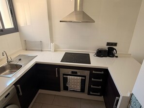 Una cocina compacta con fregadero, estufa, horno y cafetera.