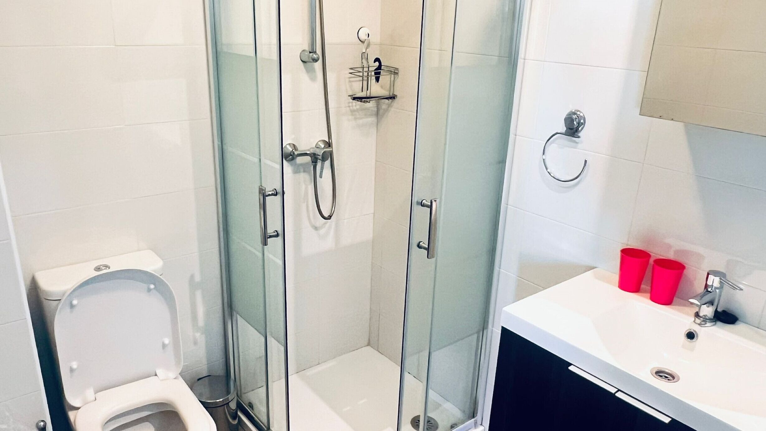 A modern bathroom with a glass-enclosed shower, a toilet, and a sink with red cups.