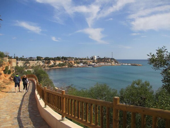 Una passeggiata costiera con ringhiera in legno, che conduce a una vista sul mare e su una cittadina con edifici e una torre.