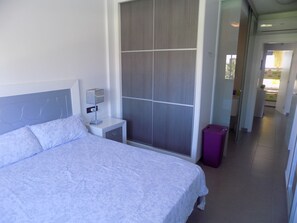 A bedroom with a bed, a nightstand, a lamp, a wardrobe, and a purple laundry basket. - Ground Floor Oasis Beach IV (Orihuela)