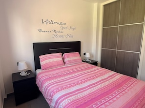 A bedroom with a bed, two bedside tables, a wall with multilingual 'Good Night' text, and a wardrobe. - Ground Floor Oasis Beach IV (Orihuela)