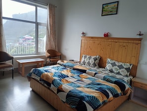 Un dormitorio con cama de madera, una silla, una mesita y una ventana con vistas al paisaje.