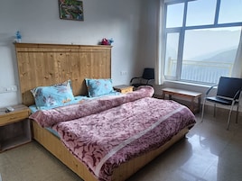 A bedroom with a wooden bed, a desk, a chair, and a window with a view.