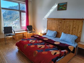 Un dormitorio con cabecera de madera, cama con ropa de cama estampada, un escritorio con silla y una ventana con vistas a un paisaje montañoso.