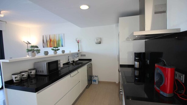 A modern kitchen with white cabinets, a black countertop, a microwave, a coffee maker, and a red appliance. - Groundfloor Tindra Punta Prima (Torrevieja)