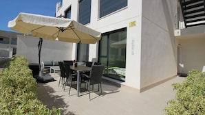 An outdoor patio with a table and chairs, a large umbrella, and a sofa. - Groundfloor Tindra Punta Prima (Torrevieja)