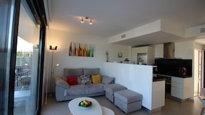 A modern living room with a grey sofa, a white coffee table, and a kitchen area in the background. - Groundfloor Tindra Punta Prima (Torrevieja)