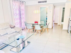 A modern living room with a glass coffee table, a sofa, and a dining area with chairs and a table. - House Tindra Homes Punta Prima (Torrevieja)