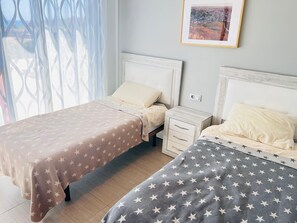 A bedroom with two beds, each with a star-patterned bedspread, a bedside table with drawers, and a framed picture on the wall. - House Tindra Homes Punta Prima (Torrevieja)