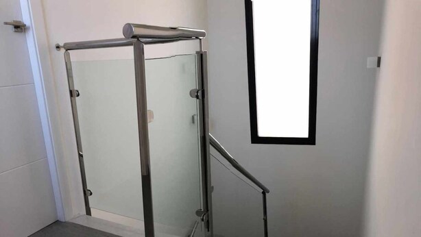 A modern staircase with a glass door and metal handrail, leading to a landing with a window. - House Tindra Homes Punta Prima (Torrevieja)