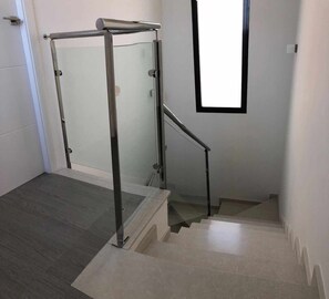 A modern staircase with a glass door and metal handrail, leading to a landing with a window. - House Tindra Homes Punta Prima (Torrevieja)