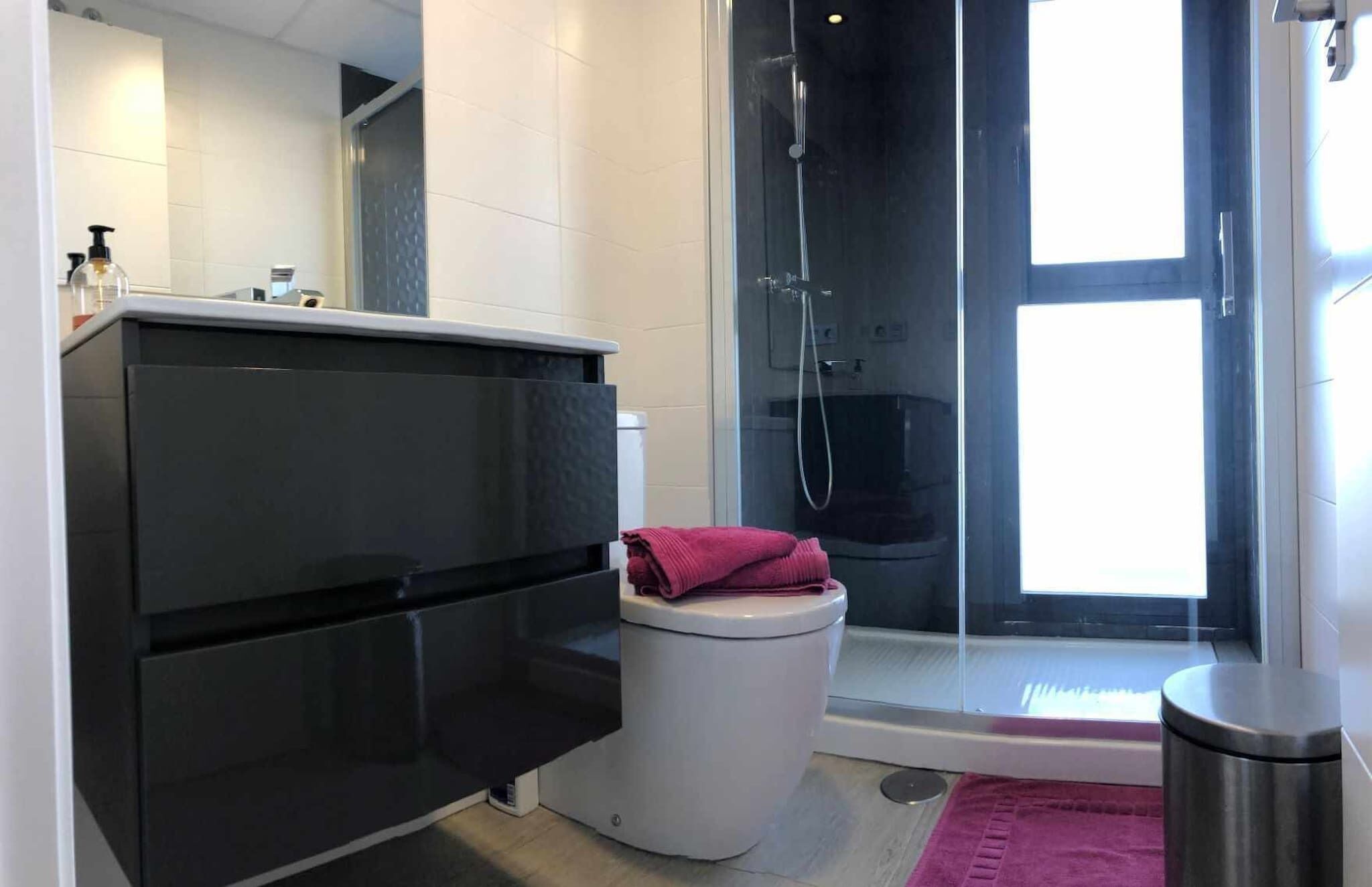 A modern bathroom with a black vanity, white toilet, and a glass shower enclosure.