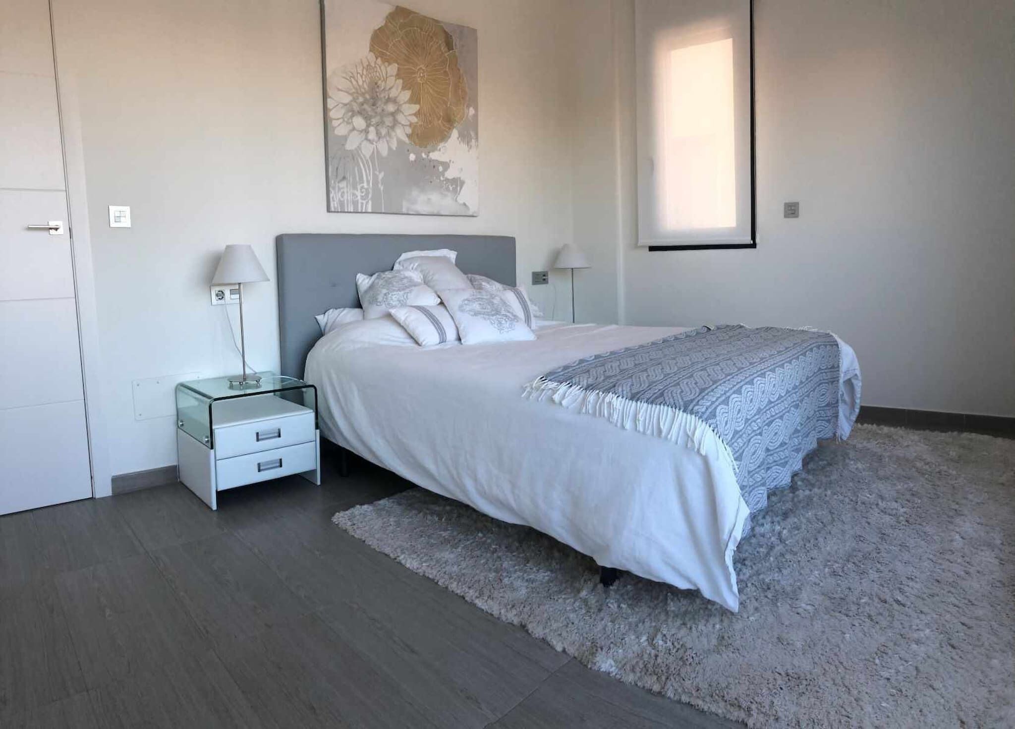 A bedroom with a bed, nightstands, a rug, and a painting on the wall.