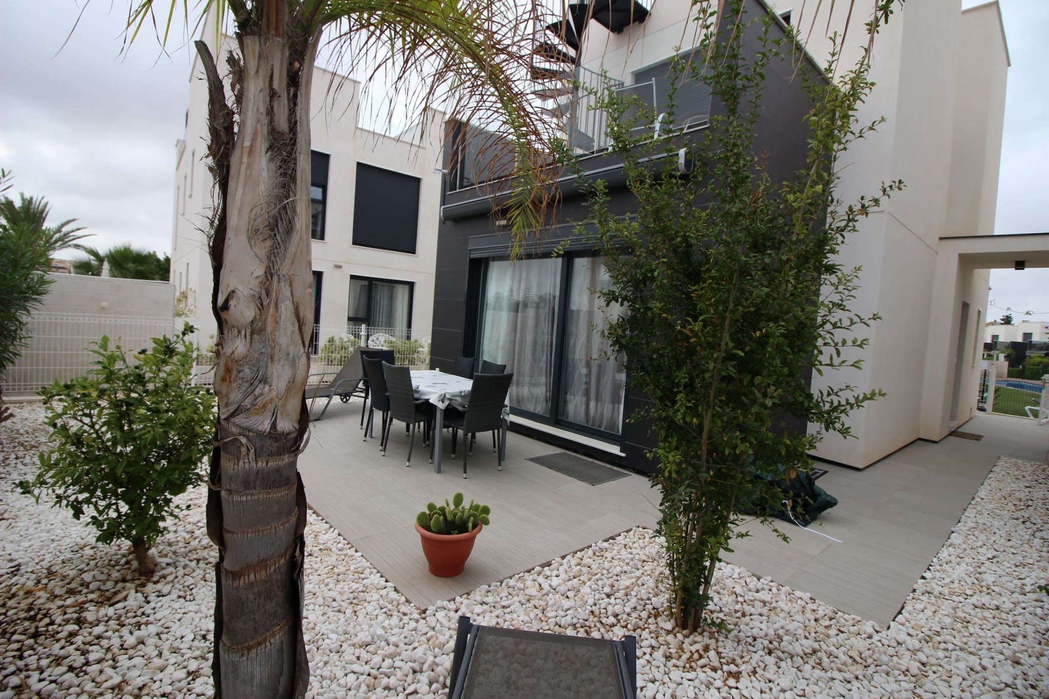 A modern outdoor patio with a dining table and chairs, surrounded by white pebbles and small plants.