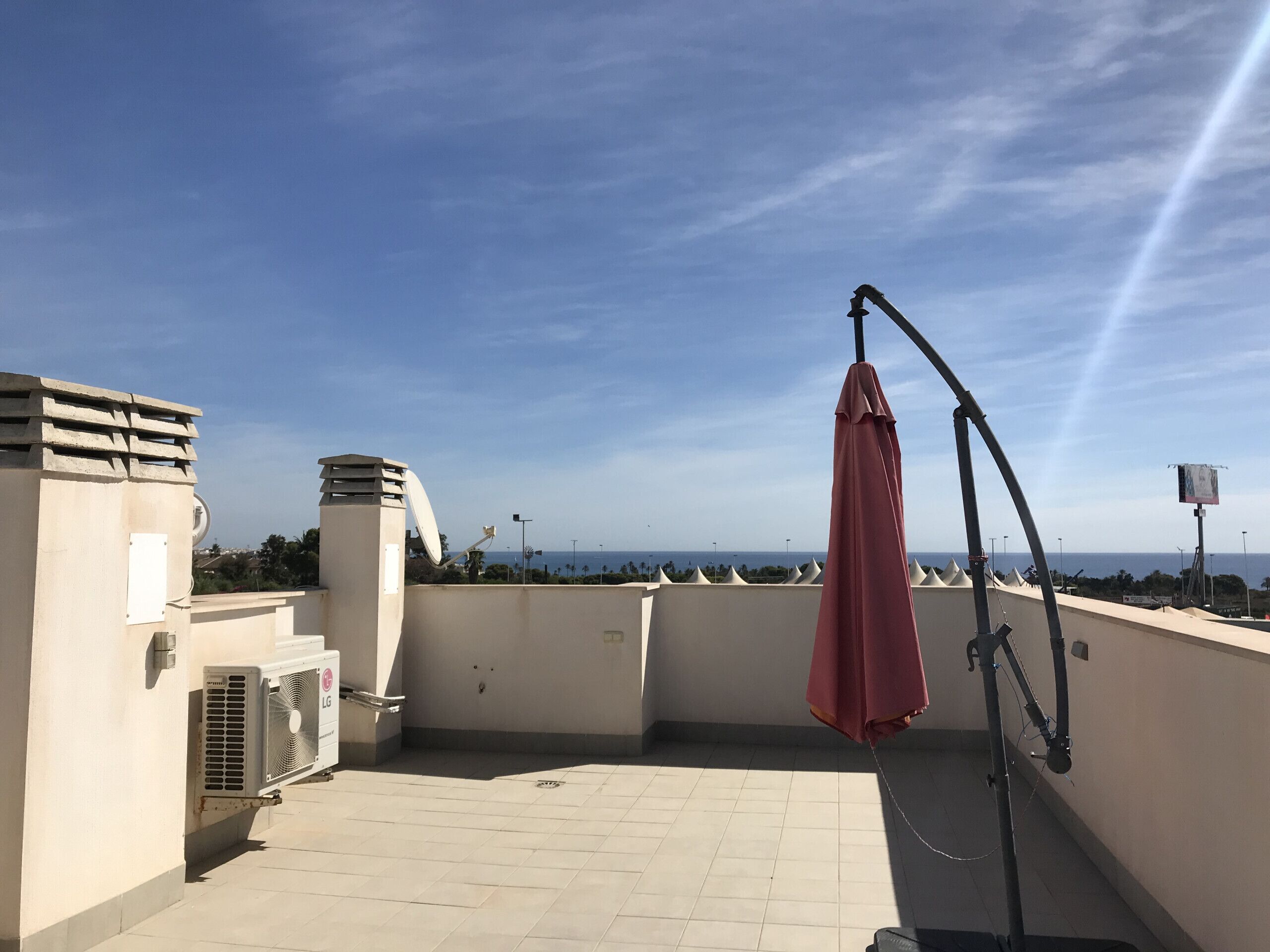 A rooftop terrace with a satellite dish, an air conditioning unit, and a red umbrella.