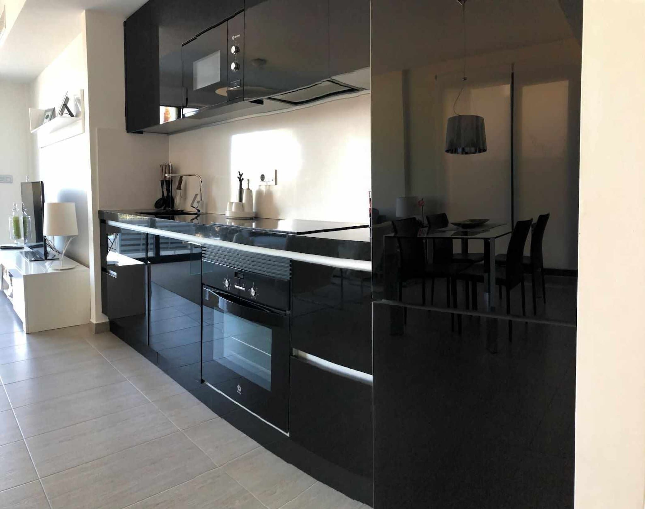 A modern kitchen with black cabinetry, a built-in oven, and a dining area with a table and chairs.