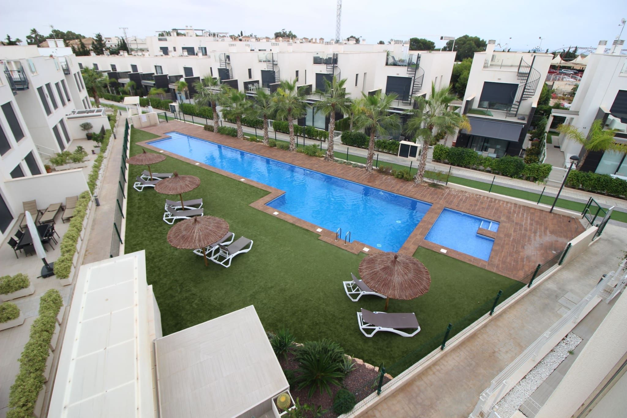 Ein Dachpool mit Liegestühlen und Sonnenschirmen, umgeben von Palmen und modernen Gebäuden.