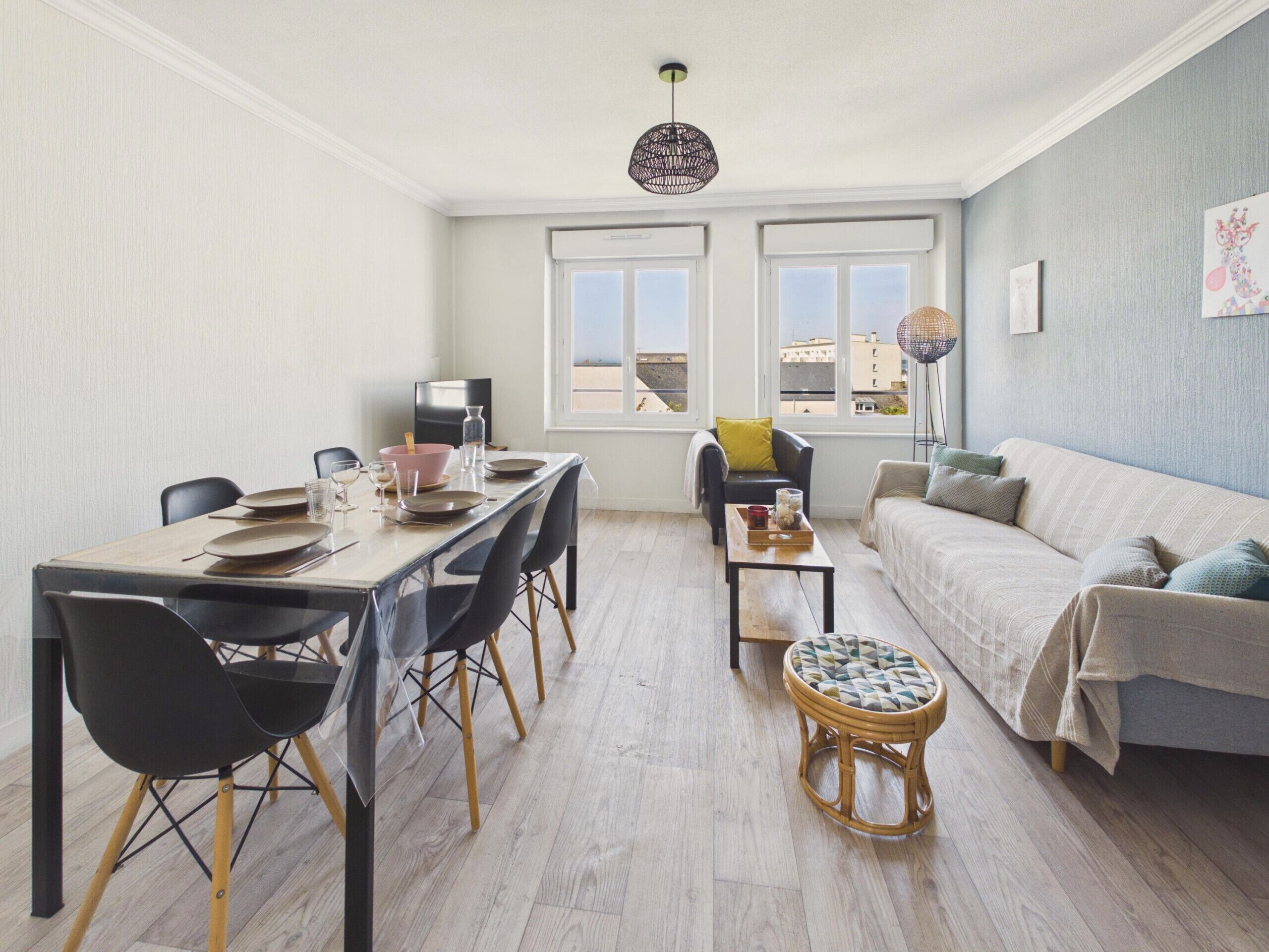 A modern living room with a dining area, large windows, and a view of buildings.