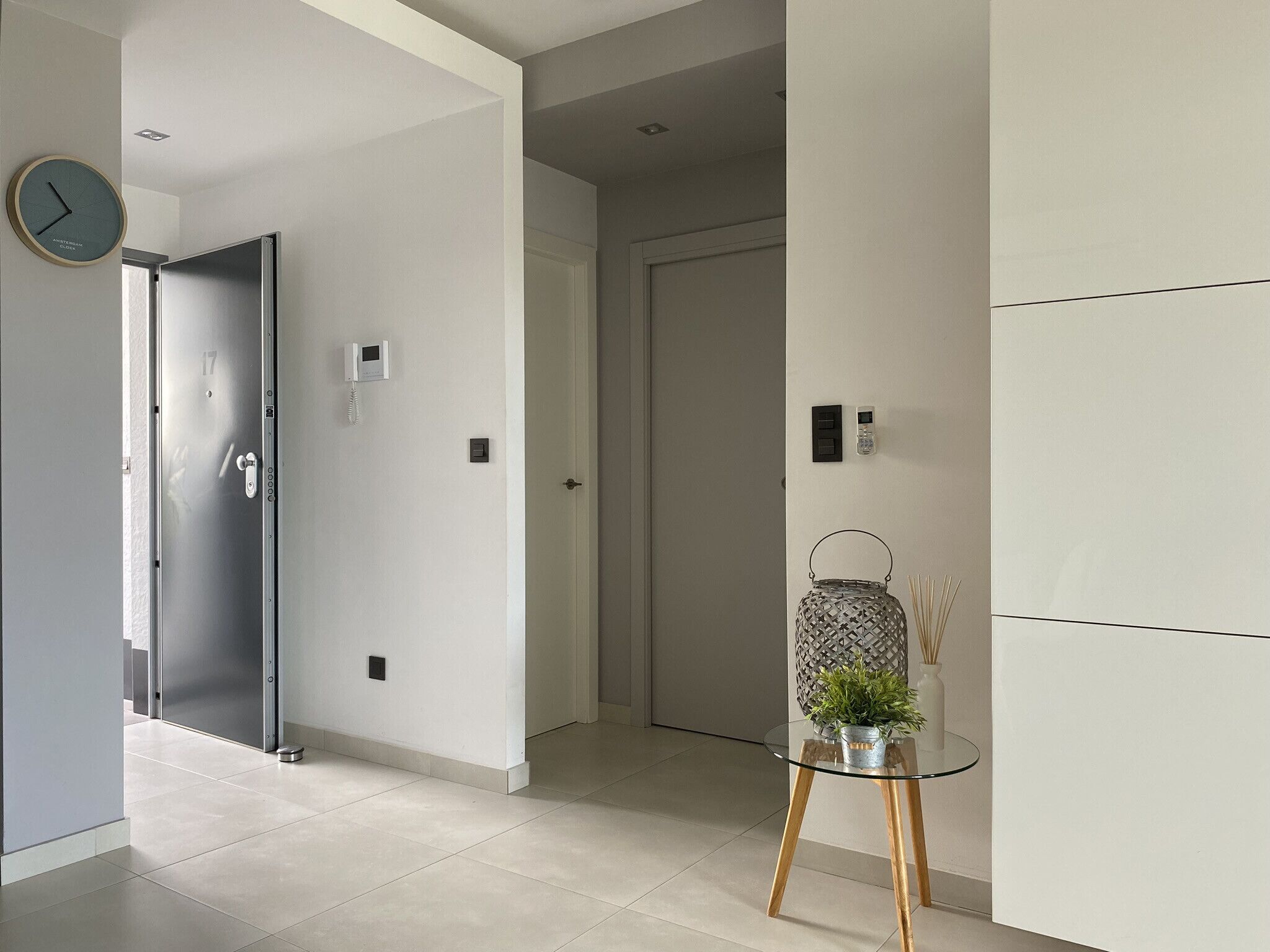 A modern hallway with a glass table, a clock, and a door with a keypad lock.