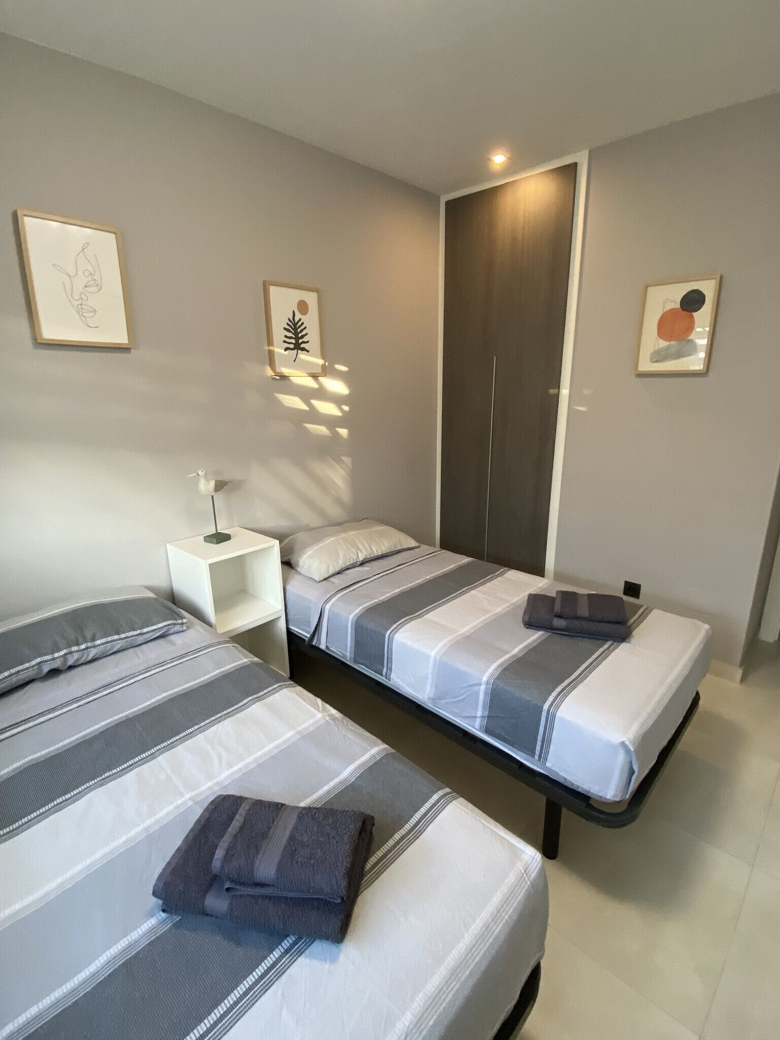 A bedroom with two beds, a nightstand, a wardrobe, and wall art.