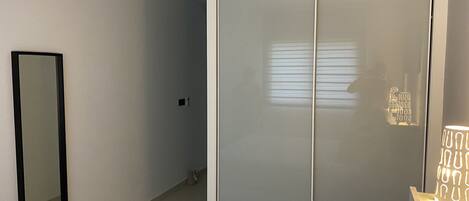 Una camera da letto con un armadio con porta scorrevole in vetro, un comodino con una lampada e uno specchio a parete.