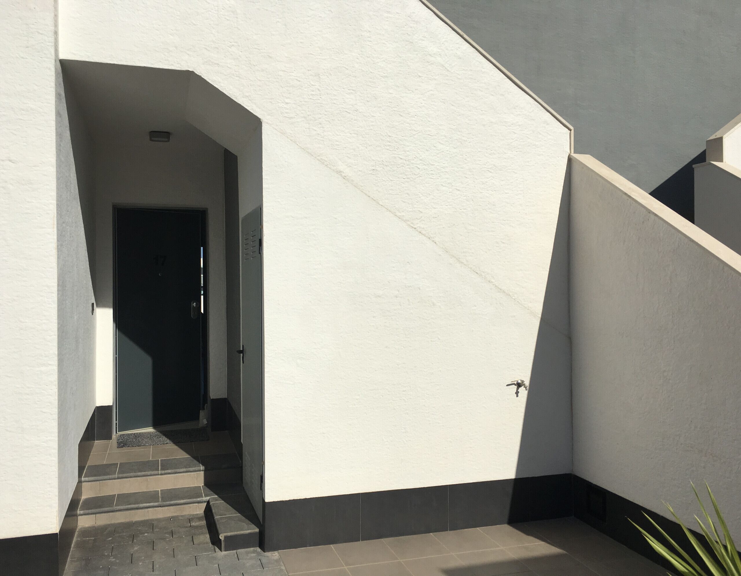 A modern building exterior with a white facade, a dark base, and a staircase leading to a door marked with the number 17.