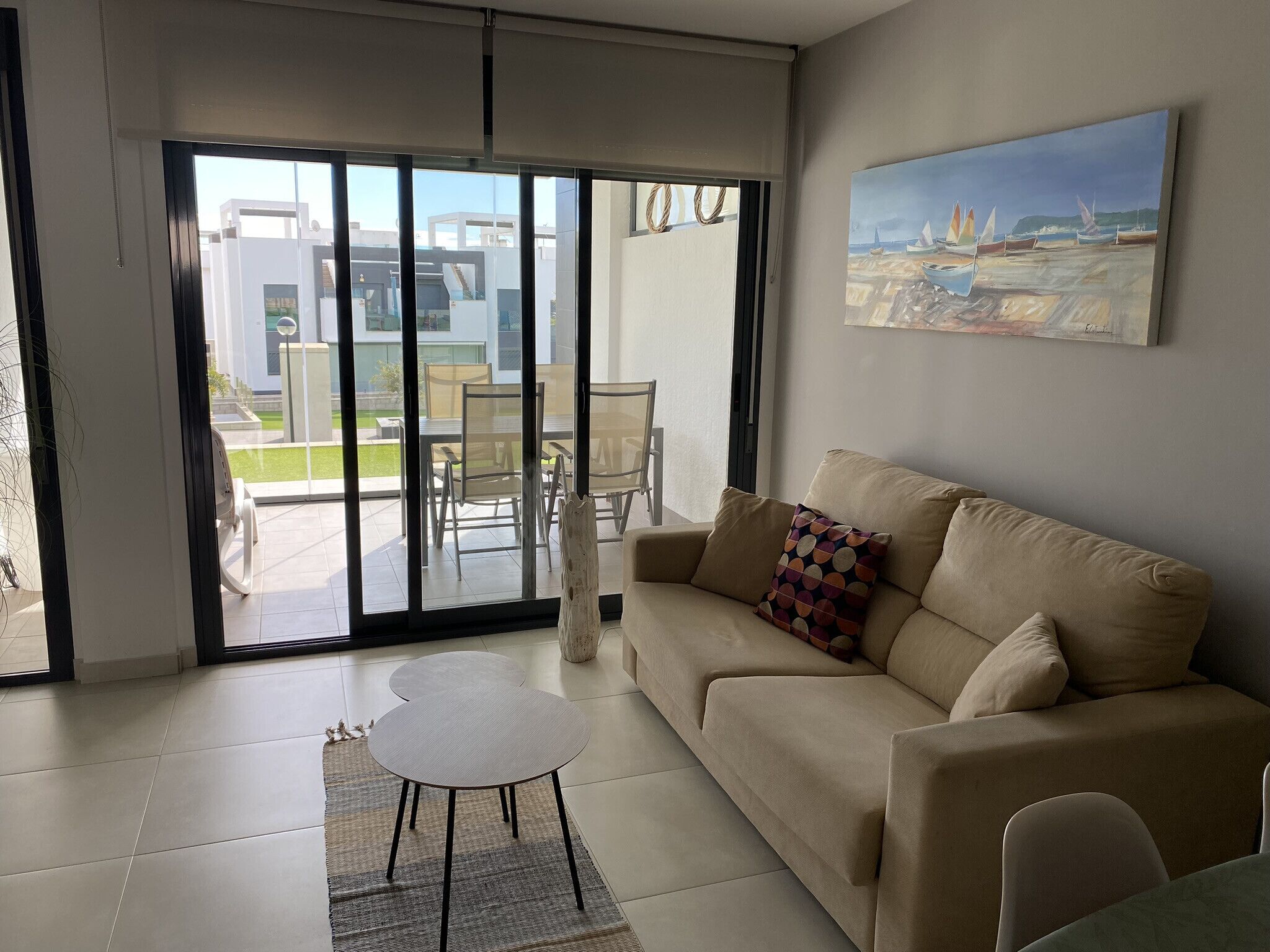A modern living room with a beige sofa, a small white table, and a glass door leading to an outdoor patio.