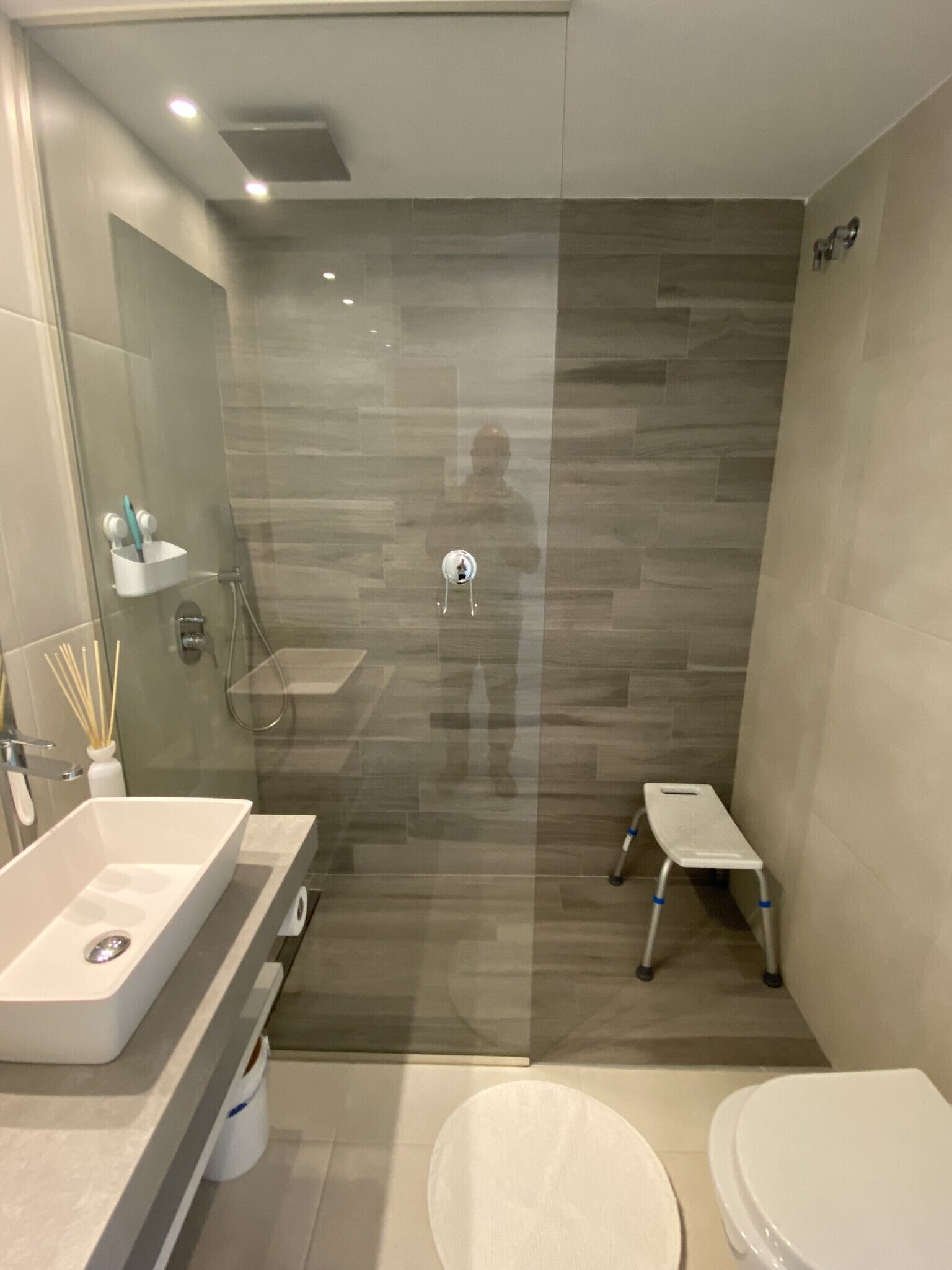 A modern bathroom with a glass shower enclosure, a white sink, and a small step stool.