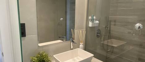 A modern bathroom with a large mirror, a rectangular sink, and a glass-enclosed shower area.