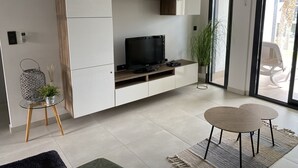 A modern living room with a flat-screen TV, a glass coffee table, and a dining area with two chairs. - Groundfloor Oasis Beach Punta Prima IX (Torrevieja)