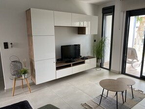 A modern living room with a flat-screen TV, a glass coffee table, and a dining area with two chairs. - Groundfloor Oasis Beach Punta Prima IX (Torrevieja)