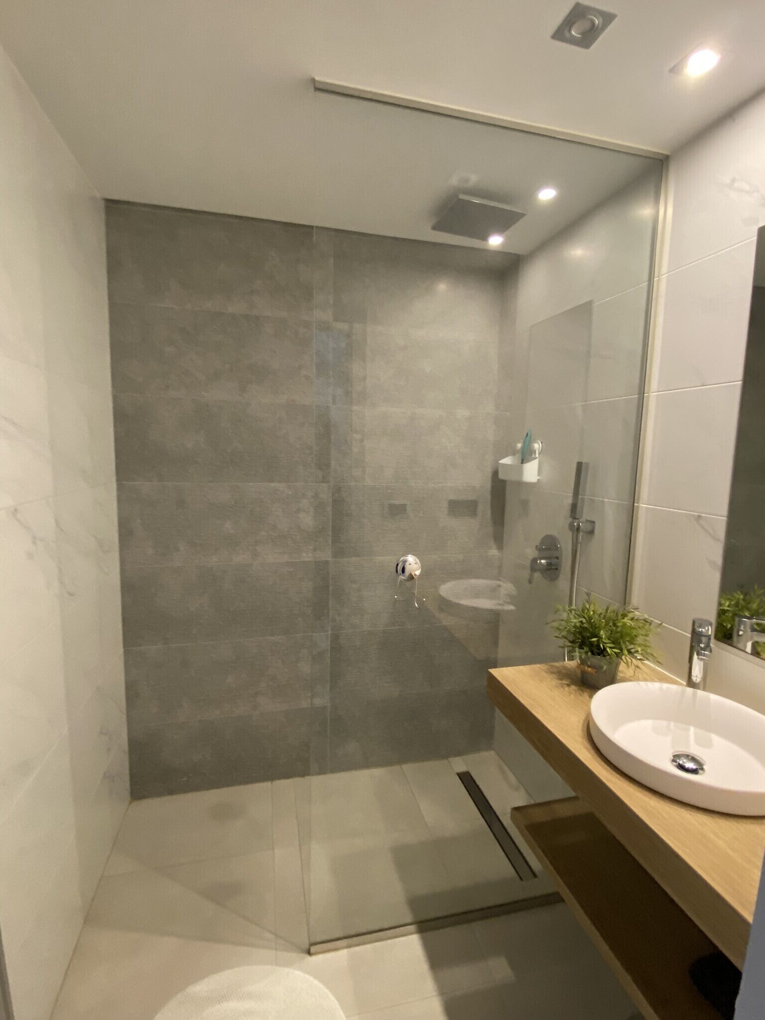 A modern bathroom with a large mirror, a sink, and a shower area.