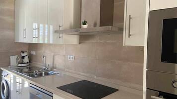 A modern kitchen with stainless steel appliances, a dishwasher, a washing machine, and a black countertop.