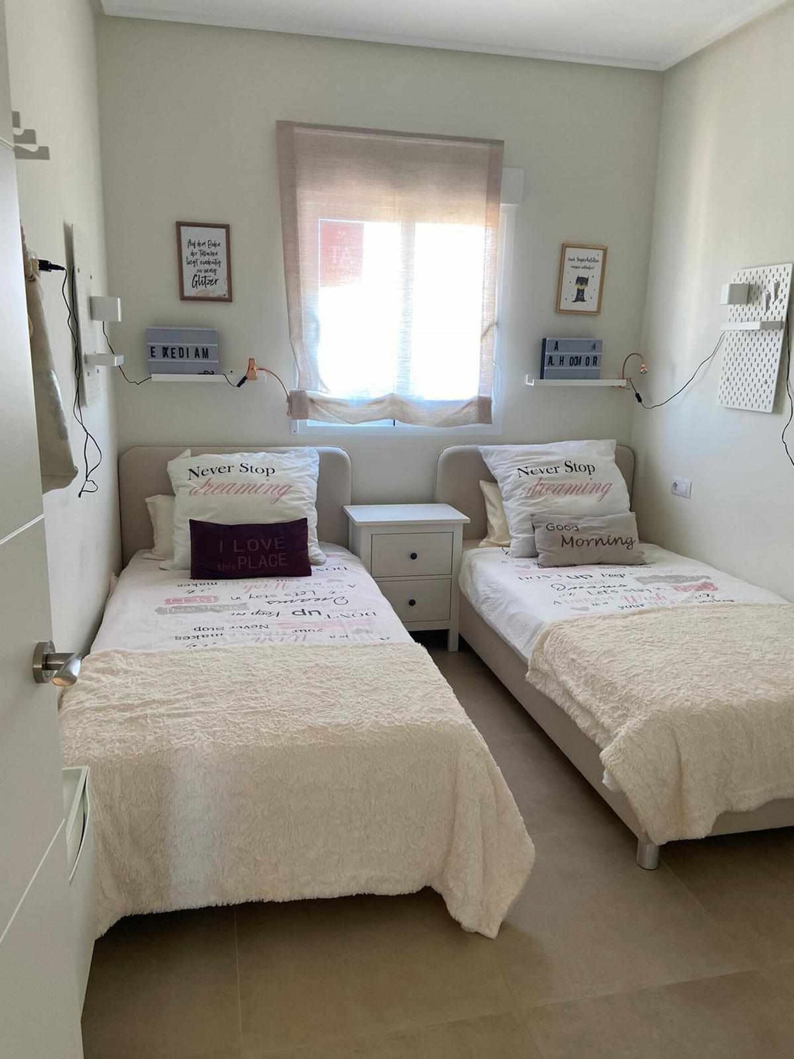 A bedroom with two single beds, a bedside table, a nightstand, and a window with curtains.