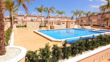 A swimming pool surrounded by palm trees and a row of apartment buildings.