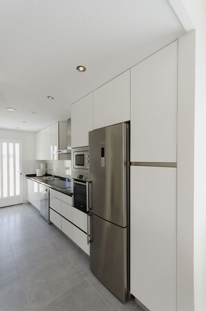 A modern kitchen with stainless steel appliances, white cabinetry, and a large window providing natural light.