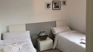 Ein Hotelzimmer mit zwei Betten, weißen Laken, einem Nachttisch mit Lampe und gerahmten Bildern an der Wand.