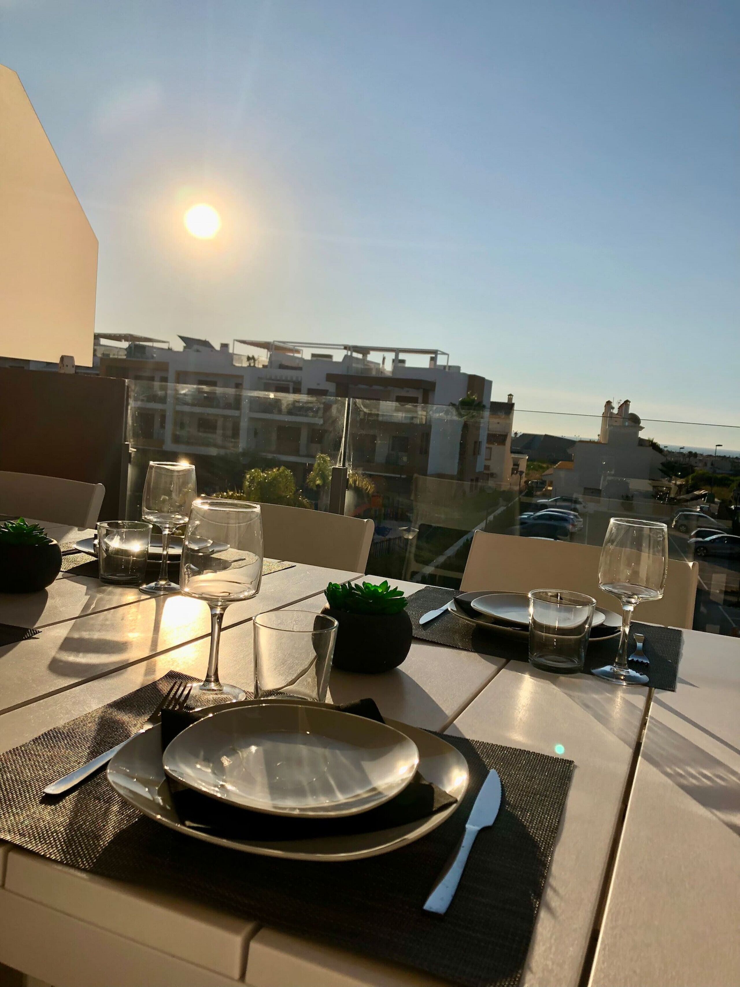 A dining table set for two with plates, cutlery, and glasses, overlooking a cityscape.