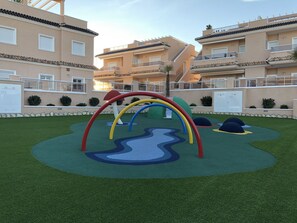 Ein Spielplatz mit einer Kletterkonstruktion in Regenbogenfarben und einem gewundenen Weg.