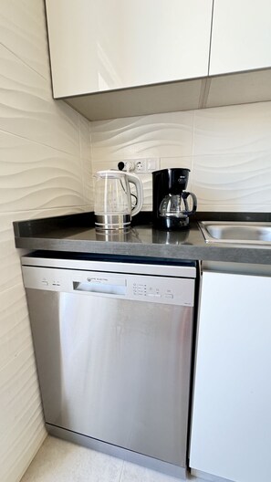 A compact kitchen with a dishwasher, a coffee maker, and a kettle on the countertop. - Penthouse Punta Prima Vistazul (Torrevieja)