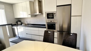Eine moderne Küche mit weißen Schränken, einem Edelstahlkühlschrank, einem eingebauten Backofen und einer Mikrowelle.