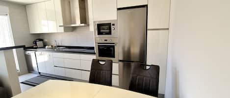 A modern kitchen with white cabinets, a stainless steel refrigerator, a built-in oven, and a microwave.