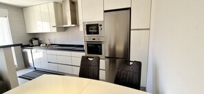 Eine moderne Küche mit weißen Schränken, einem Edelstahlkühlschrank, einem eingebauten Backofen und einer Mikrowelle.
