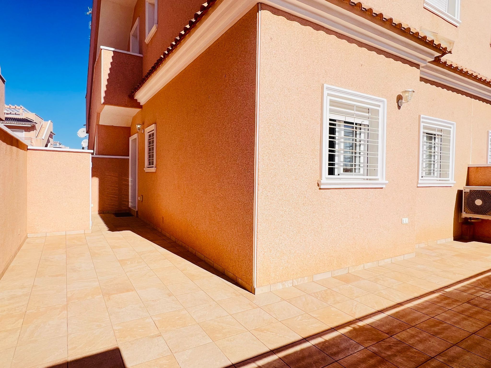 Un edificio con patio empedrado, una puerta y ventanas con contraventanas blancas.