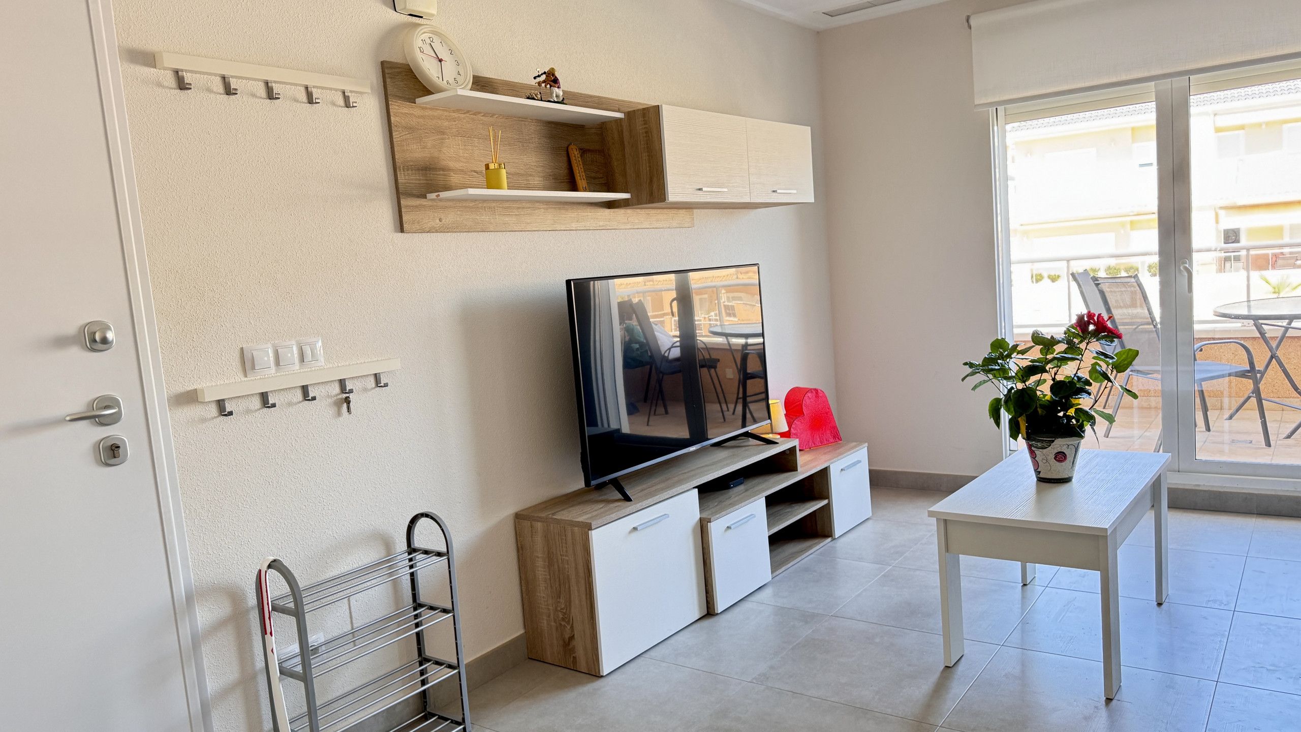 Un salon moderne avec un téléviseur à écran plat, des étagères en bois, une petite table et une plante en pot.