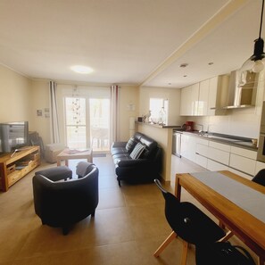 A living room with a sofa, a coffee table, and a television. There is a kitchen area with cabinets and a stove. - Penthouse Punta Prima Vistazul (Torrevieja)