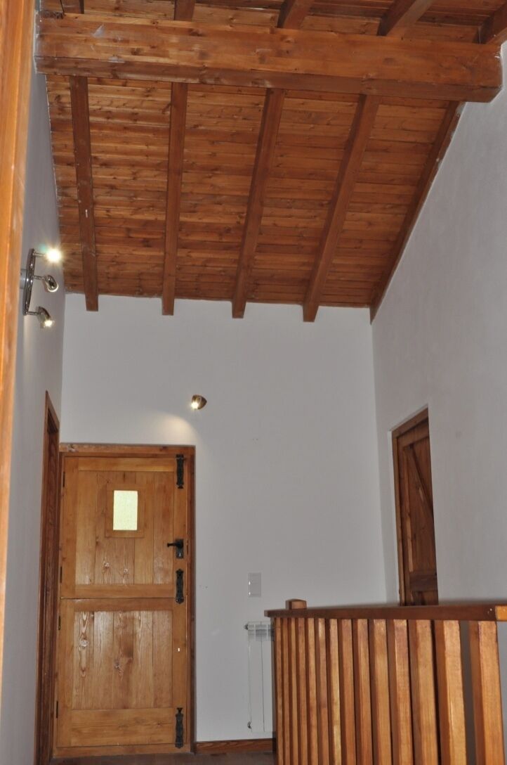 Eine Holzbalkendecke, eine Holztür mit kleinem Fenster und eine weiße Wand mit Lichtschalter.