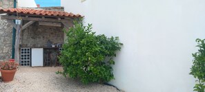 Un patio con un muro de piedra, un cubo metálico, una planta en maceta y un muro blanco.