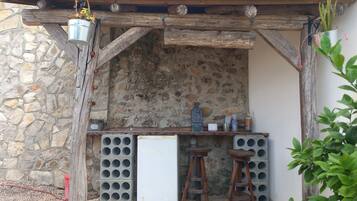 A rustic outdoor bar area with a stone wall, wooden beams, and a chalkboard menu.