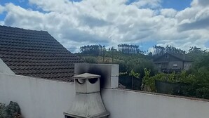 A concrete outdoor grill structure with a chimney, surrounded by a gravel area and a white wall. - Casa De Campo De Oliveiras (Penela)